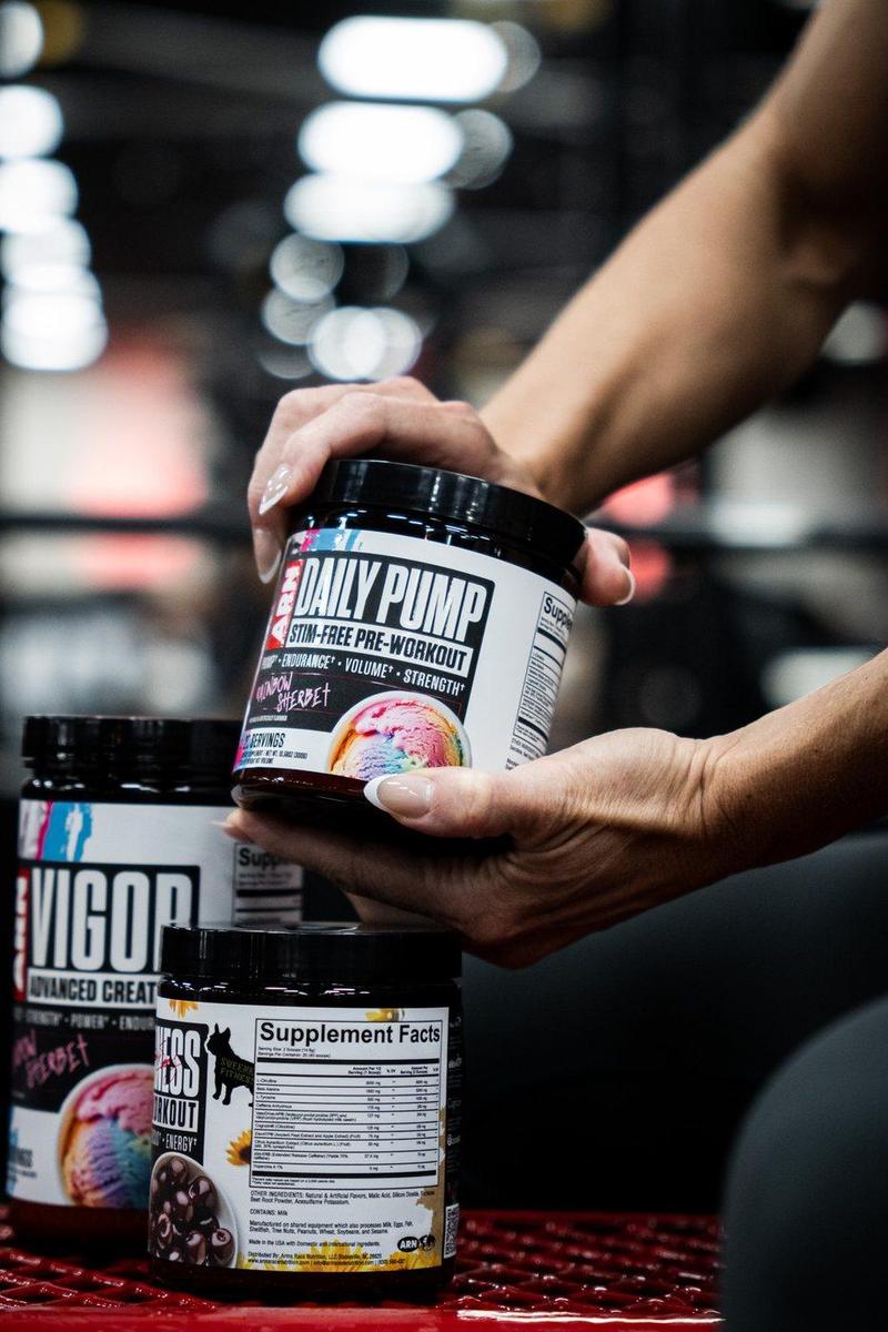 Hands lifting a tub of ARN Daily Pump off a stack of supplements