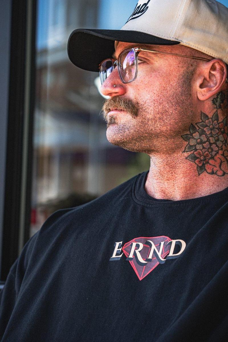 Tattooed athlete in a cap and glasses looking off frame in an ERND diamond tee