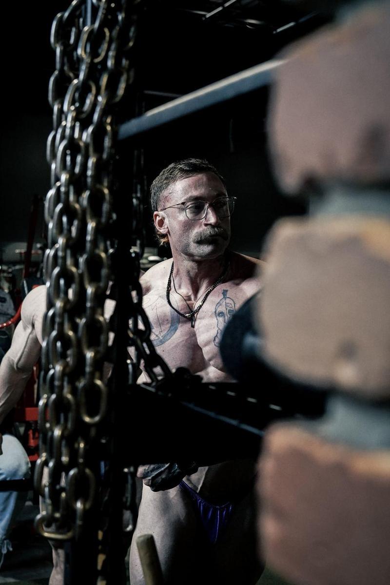 Bodybuilder framed by hanging chains in a dark gym