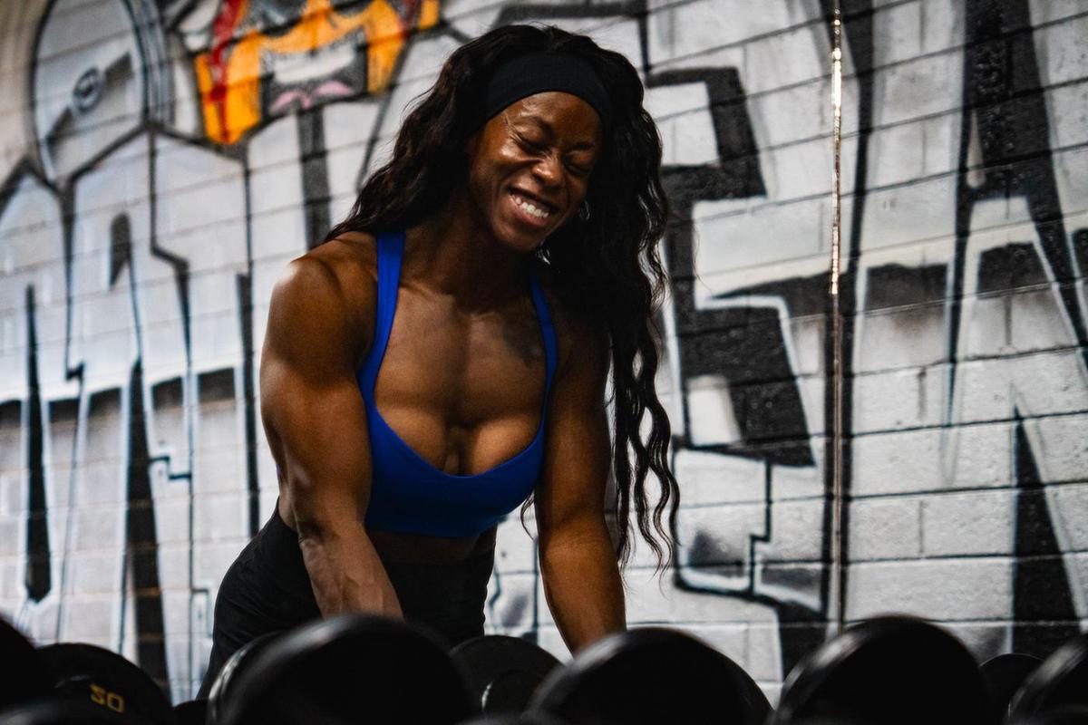 Female athlete laughing at a dumbbell rack in front of a graffiti wall