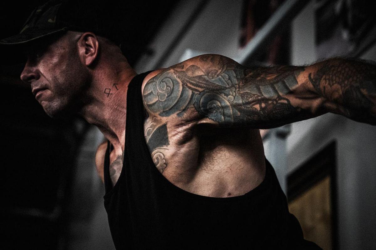 Tattooed lifter in a tank stretching his arm back
