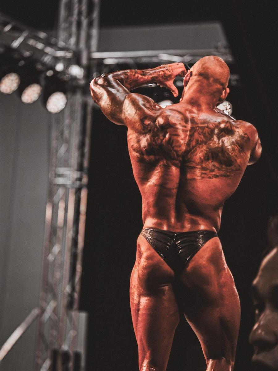 Tattooed bodybuilder hitting a back pose under stage lights